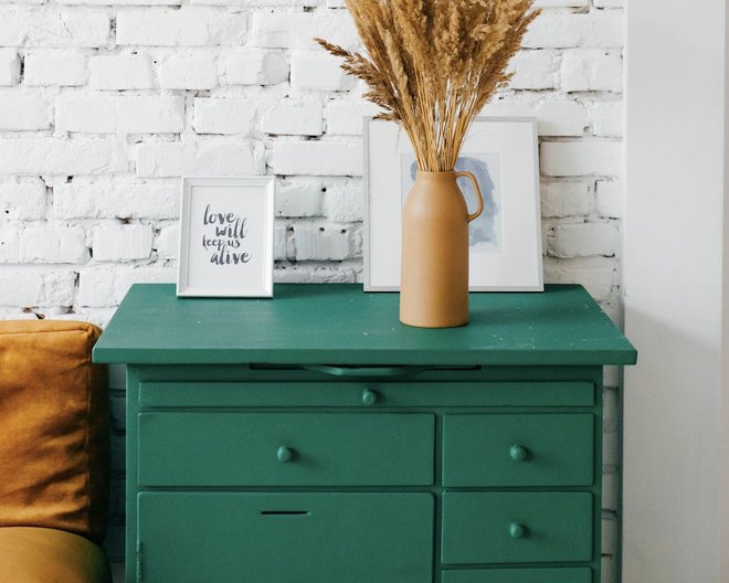 Picture of a green cupboard and a flower vase placed on top with two photo frames